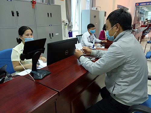 Cán bộ BHXH tỉnh hướng dẫn anh Lò Văn Hải (xã Pha Mu, huyện Than Uyên) làm thủ tục cấp lại thẻ BHYT tại Trung tâm Phục vụ hành chính công tỉnh.